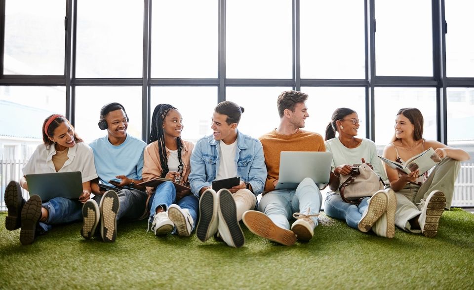 A group of people sitting together with laptops and notebooks smiling