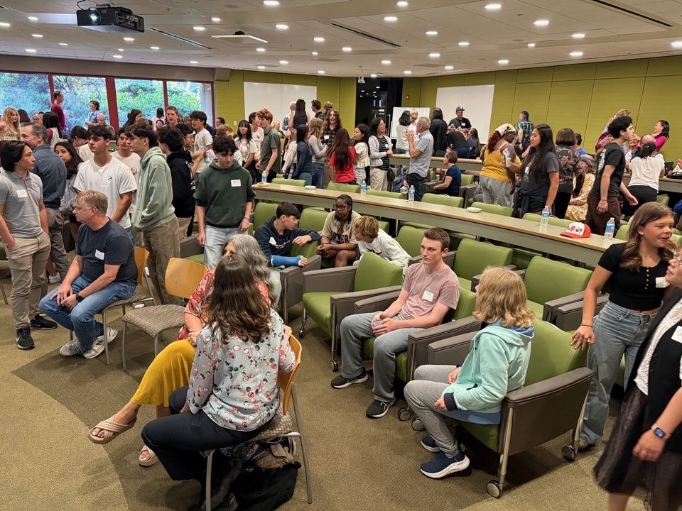 a group of students in a classroom mingling and talking to each other