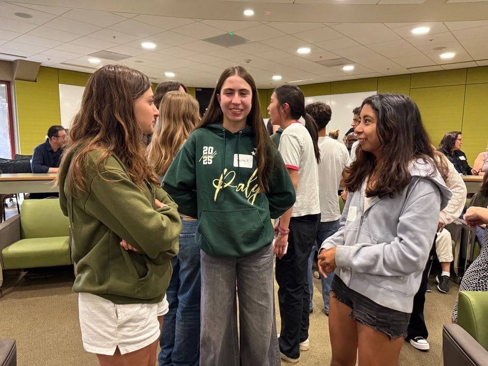 three female students standing together holding a conversation and smiling