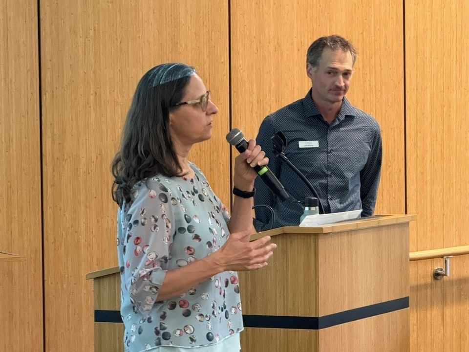 two adults at a podium, male and female, the female is speaking on a microphone