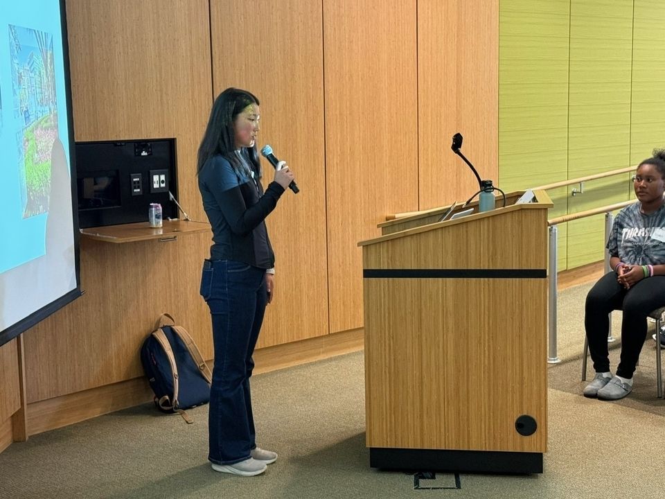 A female student with dark hair standing at a podium with a microphone in hand