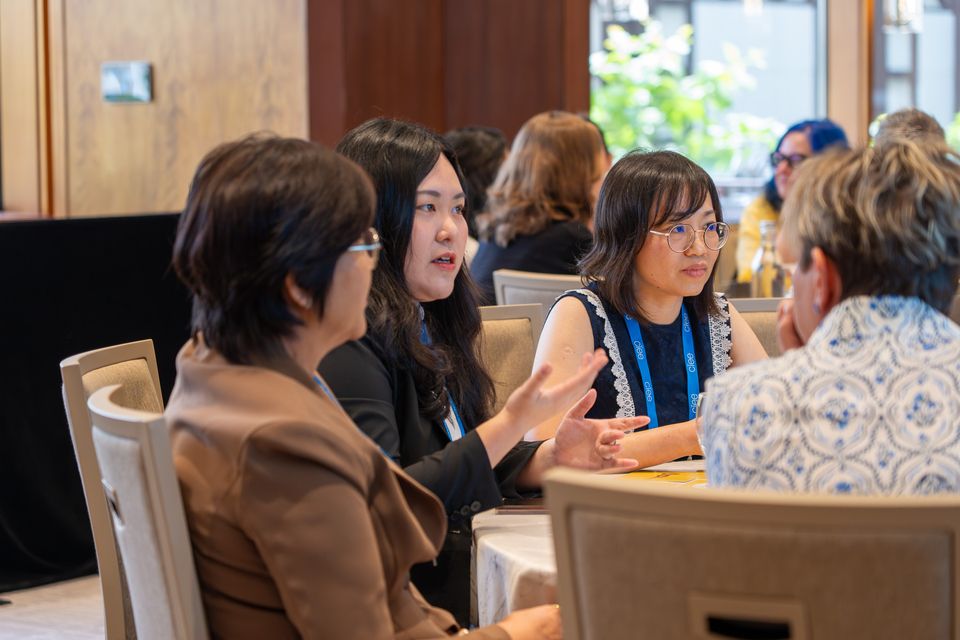 5 women seated at a table discussing together