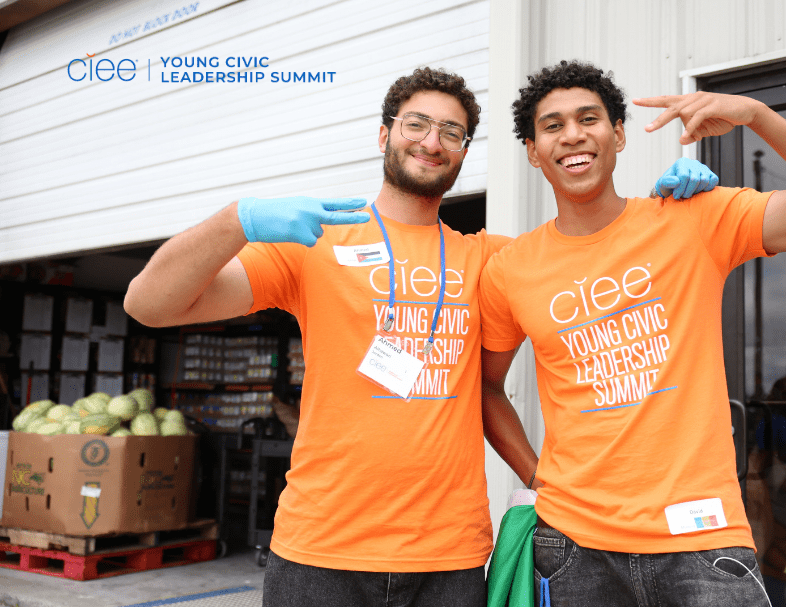 2 young men pose together and put up a peace sign with orange shirts on that say "young civic leadership summit"
