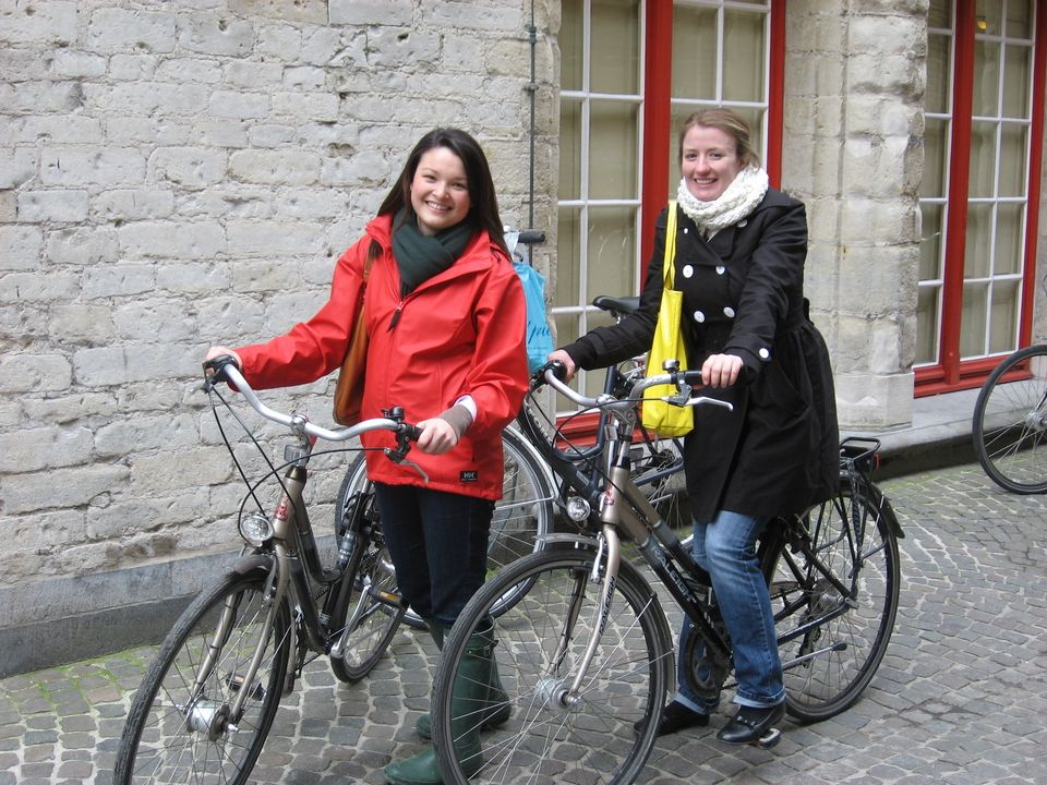 Two female students riding bicycles over cobblestone streets in Brussels, Belgium