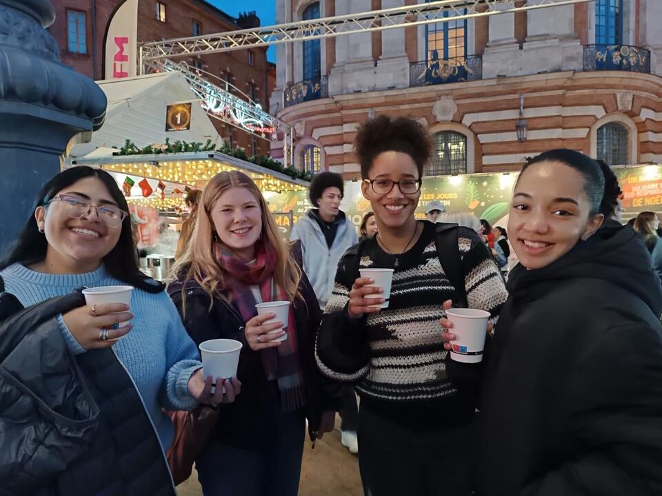 Group of 4 girls pose with hot drinks at Toulouse Christmas market